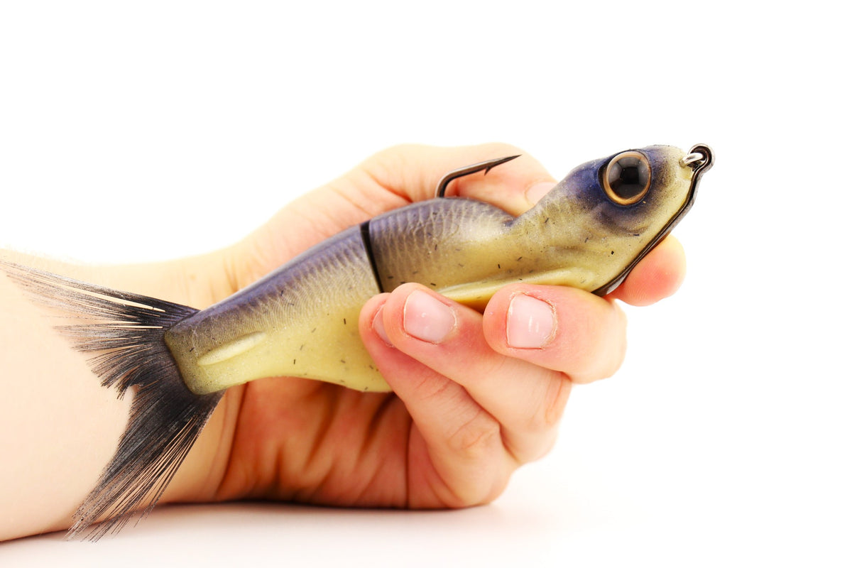 Durable Soft Dad silicone glide bait in Dry Bones color held in hand showing its flexible jointed body and brushed fiber tail.